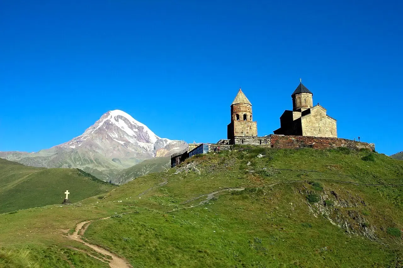 Gergeti Trinity Church on a green ridge with snow-capped Mount Kazbek behind
