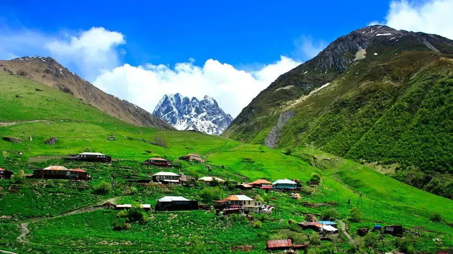 Juta village on green slopes with the rocky Chaukhi peaks behind
